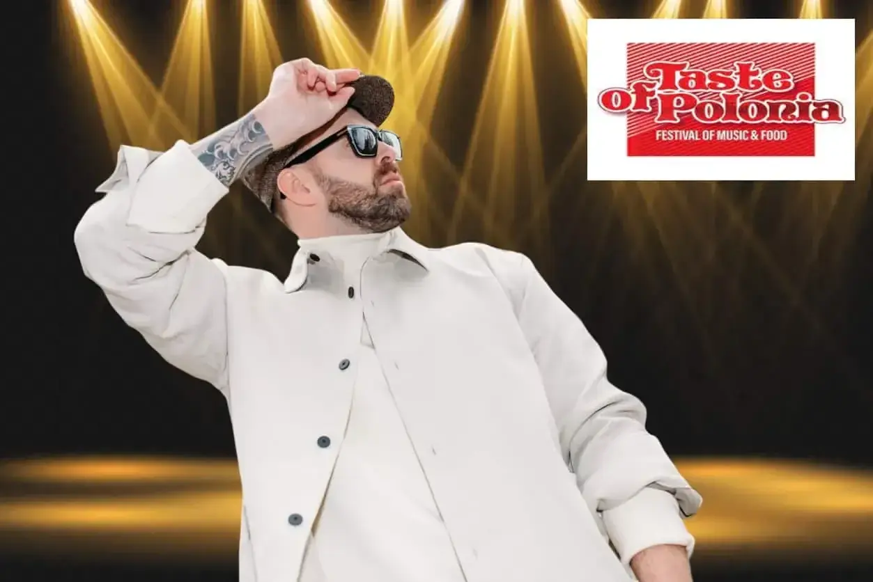 Grzegorz Hyży wstaje na scenie Taste of Polonia, w białej kurtce i czapce, w blasku reflektorów.