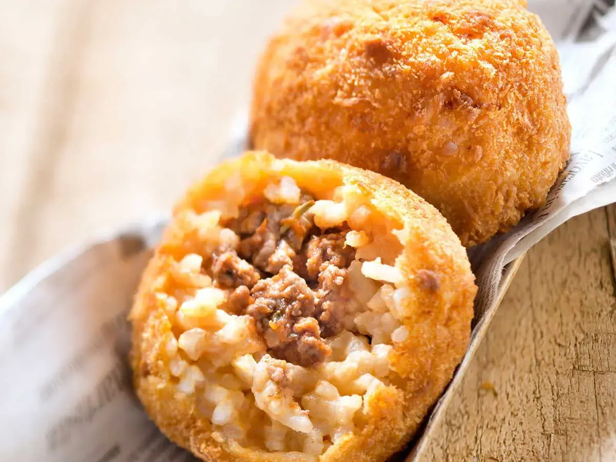 Deux arancini bolognaise dorés et croustillants, l'un ouvert révélant un cœur de riz et de viande savoureux.