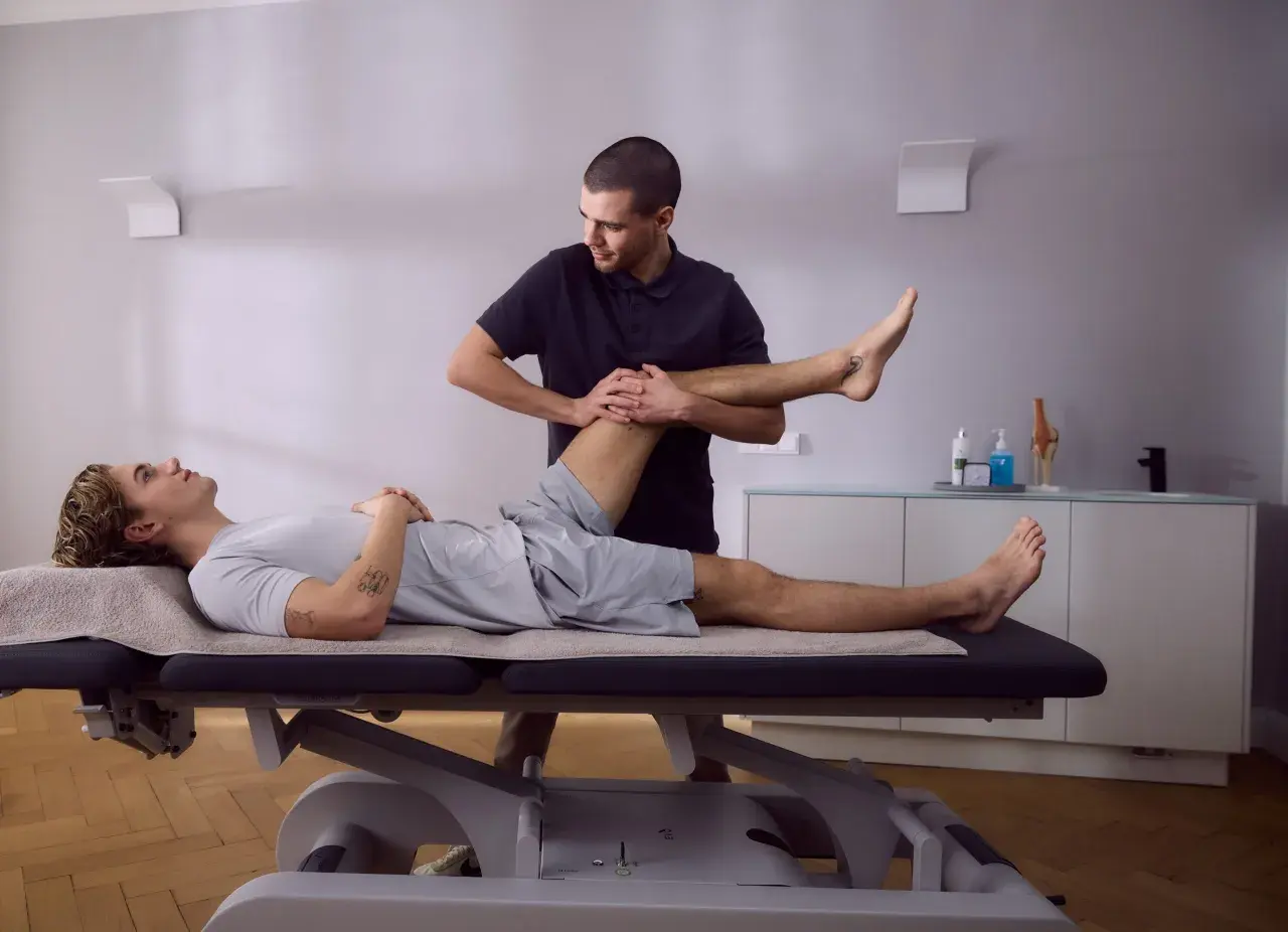 Physiotherapeut dehnt das Bein eines Patienten auf einer Liege. Die Knie-Schiene nach OP wird sanft bewegt, um die Beweglichkeit wiederherzustellen.
