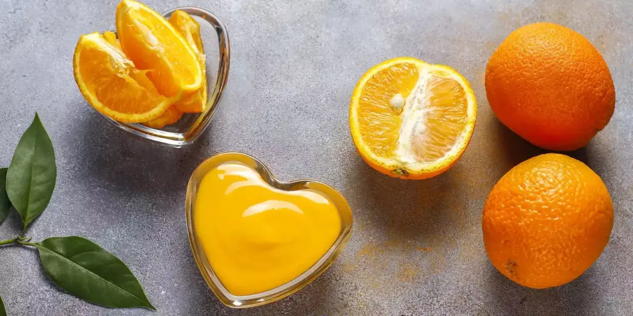 Arance fresche, spicchi e succo in ciotole a forma di cuore. Scopri quale alimento contiene più vitamina C per un cuore sano!