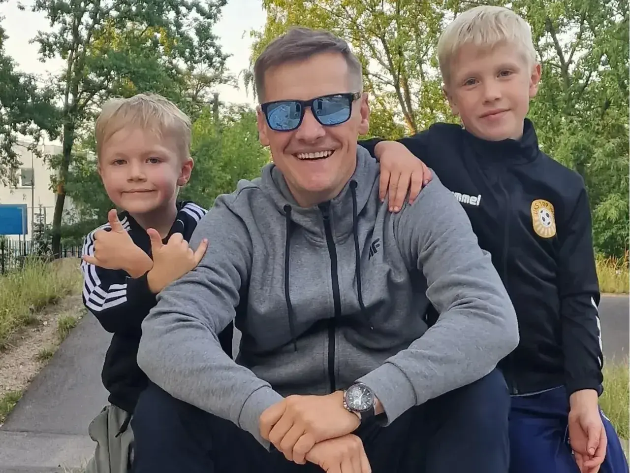 Marcin Mroczek z uśmiechem i dwoma synami, którzy go obejmują. Radosny dzień ojca i dzieci.