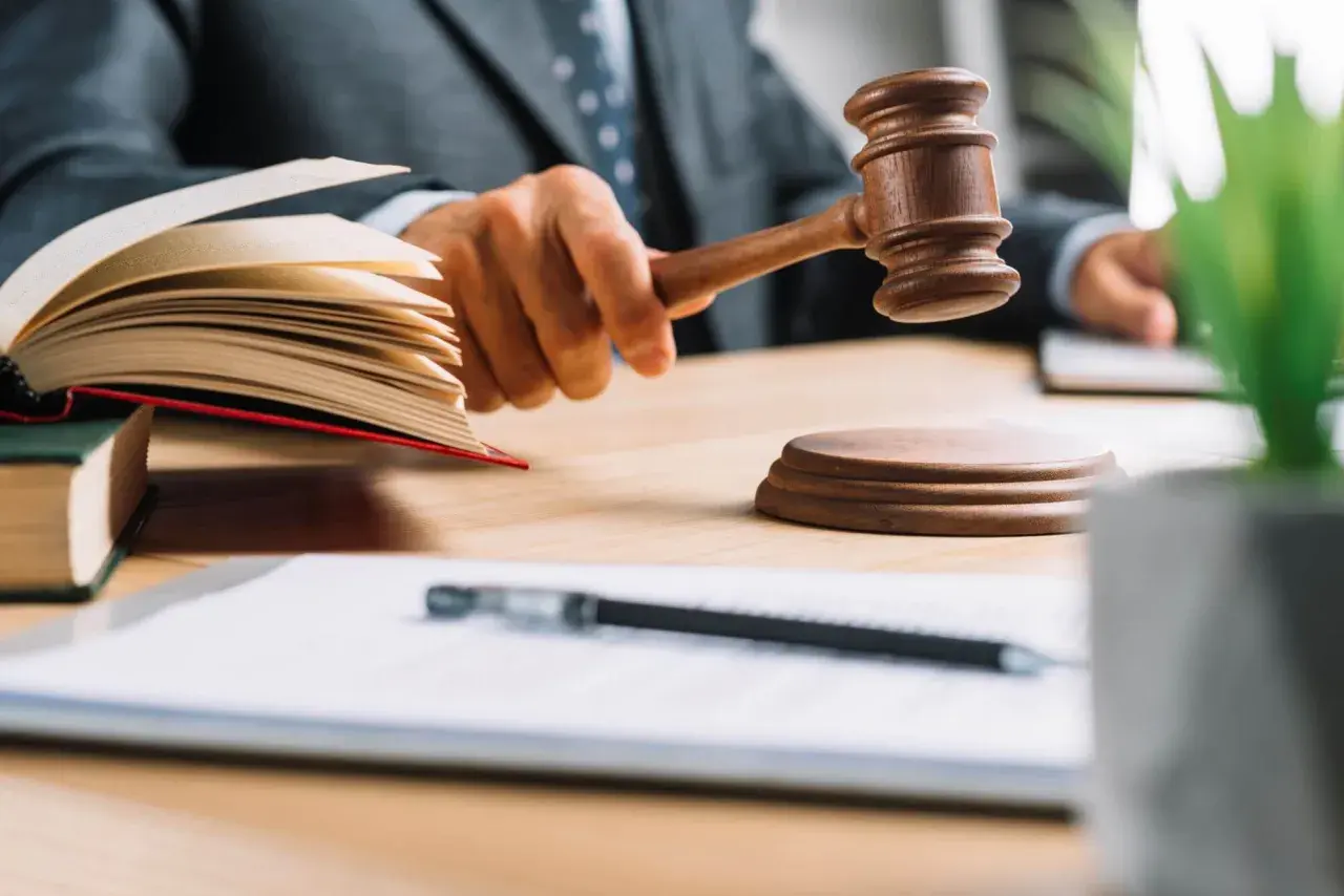 Sędzia uderza młotkiem, ogłaszając wezwanie do udziału w sprawie spadkowej. Na stole księgi i dokumenty.