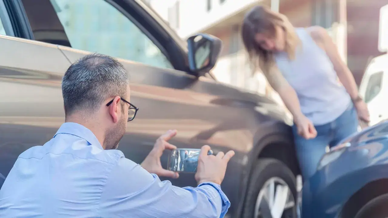 Man fotograferar parkeringsskada. Kvinnan undersöker skadan, en parkeringsskada smitning.