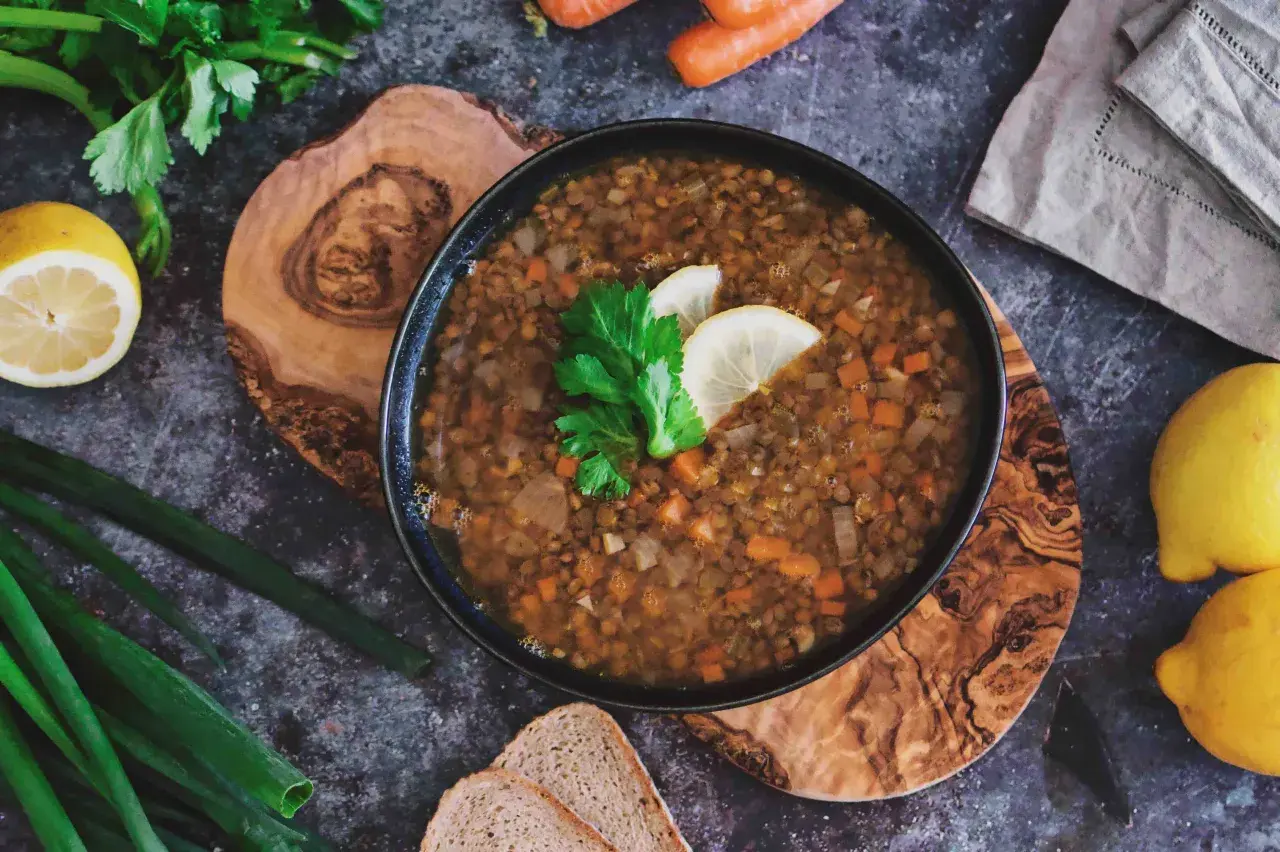 Herzhafte italienische Linsensuppe mit Karotten und Sellerie, garniert mit Zitrone und Petersilie, daneben Brot und frische Kräuter.