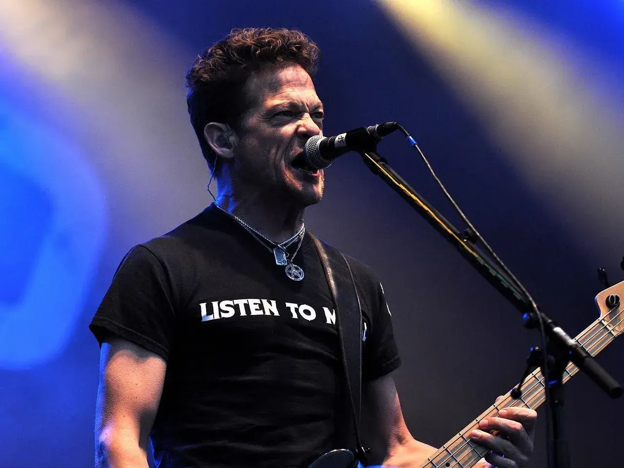 Jason Newsted z zespołu, w czarnej koszulce z napisem "LISTEN TO N", śpiewa do mikrofonu, grając na basie.