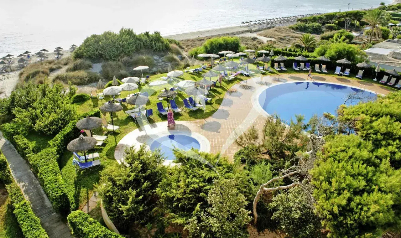 Einladende Pools und Liegen am Strand des Grupotel Natura Playa. Sonnenschirme spenden Schatten.