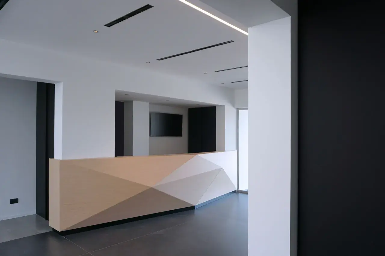 Moderno bancone reception in cartongesso con pannelli geometrici in legno chiaro.