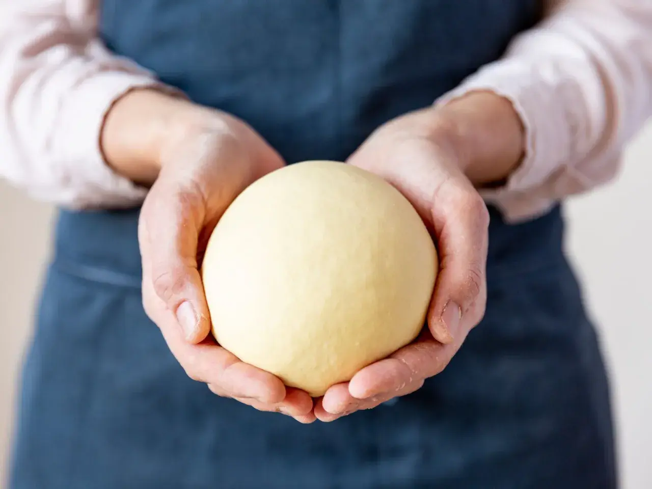Hände halten einen glatten, gelben Ball aus nudelteig ohne ei.