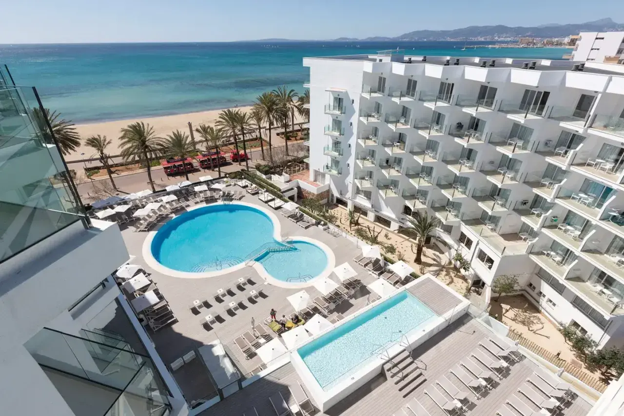 Ein modernes Hotel mit Pools und Liegestühlen, daneben ein Strand mit Palmen und dem Meer. Ein tropischer Traum!