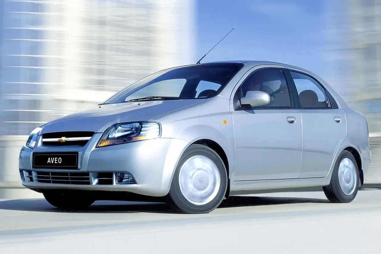 Srebrny Chevrolet Kalos, model Aveo, pędzi po drodze, rozmywając tło.