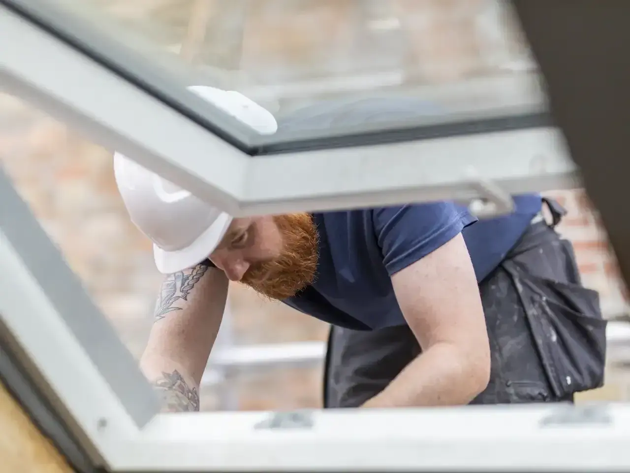 Handwerker mit Bart und Helm dichtet provisorisch das Dach ab.