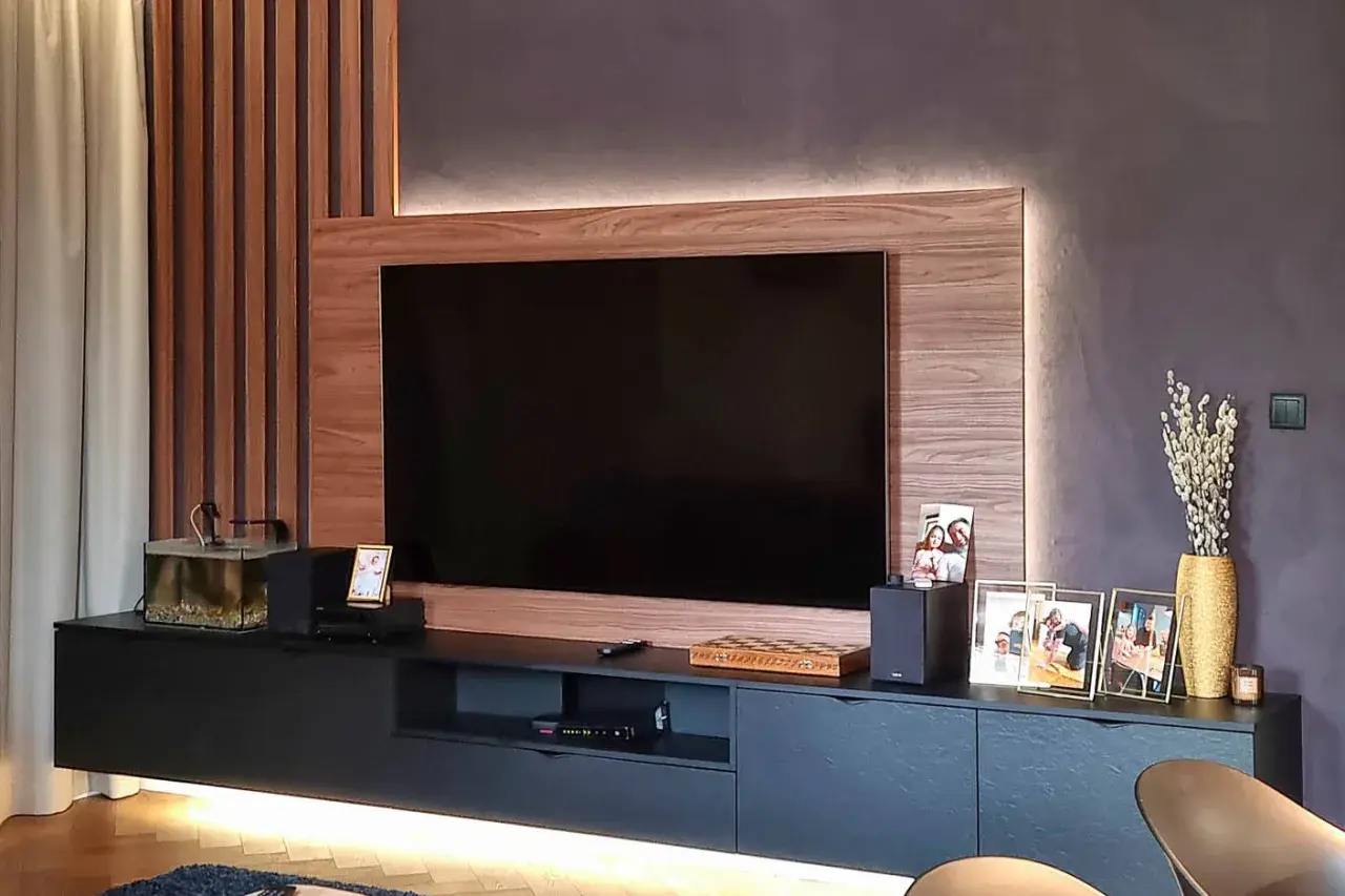 Nowoczesny salon z telewizorem w zabudowie meblowej. Drewniane panele i subtelne podświetlenie tworzą przytulną atmosferę.