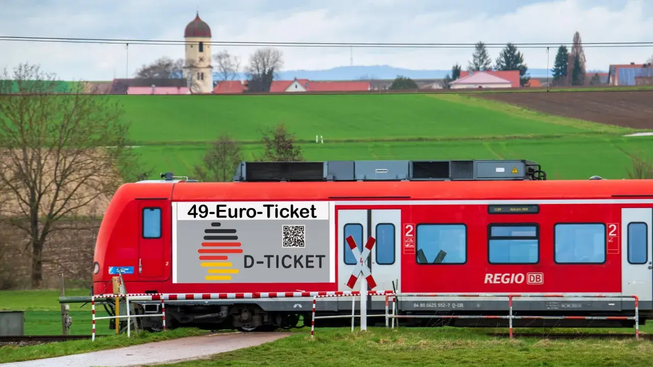 Rote Bahn mit "49-Euro-Ticket" Aufdruck fährt durch ländliche Gegend. Das rrx deutschlandticket macht Reisen günstig.