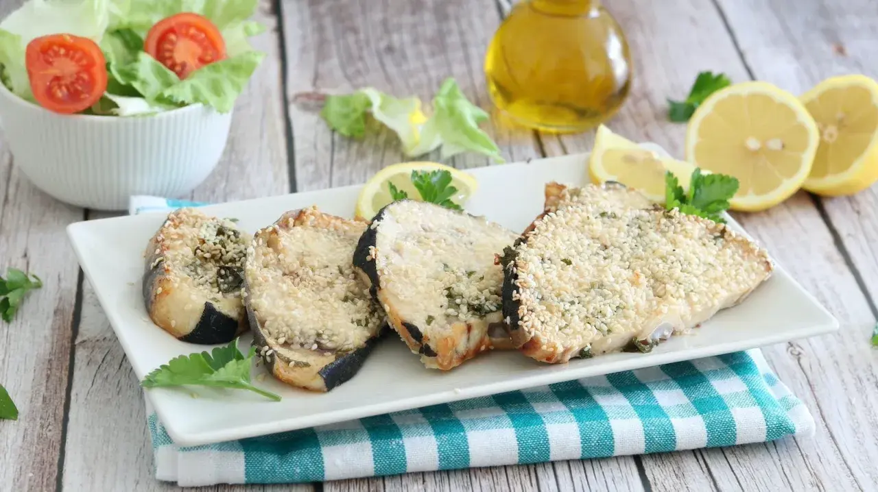 Fette di pesce spada in friggitrice ad aria, impanate con semi di sesamo e erbe aromatiche, servite con limone e insalata.
