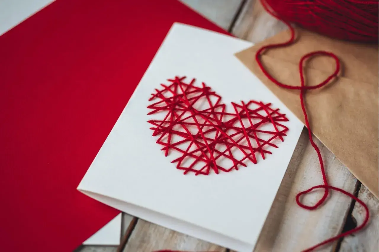 Eine selbstgemachte Valentinstagskarte mit einem roten Herz aus Garn. Perfekt zum Valentinstagskarte basteln.