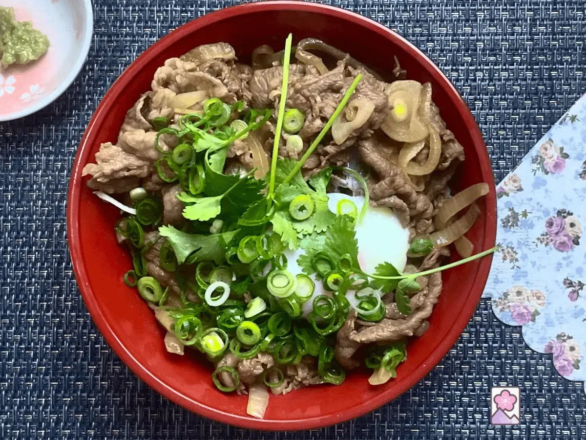 A delicious wagyu donburi with thinly sliced beef, onions, and a perfectly poached egg, garnished with fresh scallions and cilantro.