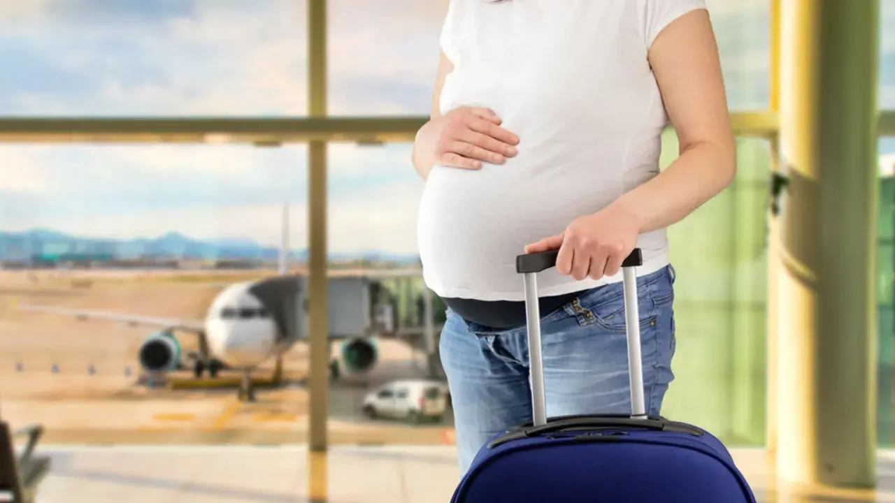 Ciężarna kobieta z walizką na lotnisku, gotowa do podróży. Wygląda na to, że jest fit to fly.