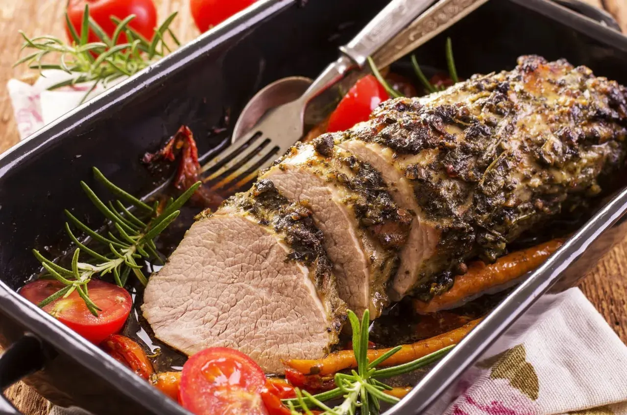 Un délicieux roti de veau aux herbes, servi dans un plat avec des tomates cerises et du romarin.