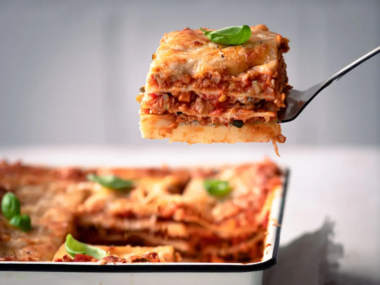 Ein Stück köstliche vegetarische Lasagne wird aus einer Auflaufform gehoben. Frisch, herzhaft und mit Basilikum garniert.