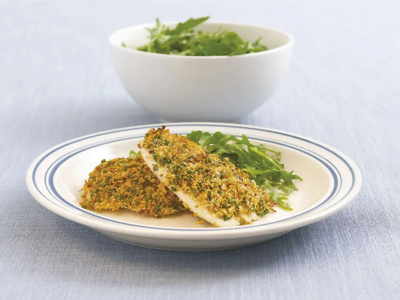 Zwei Filets Fisch mit knuspriger Parmesankruste und Rucola auf einem Teller.