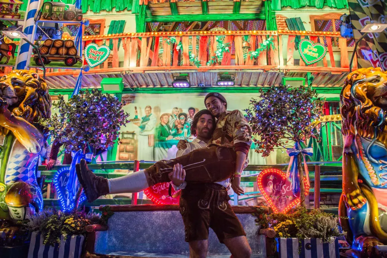 Ambiance de fête de la bière allemande : un homme porte un autre enlacé, entourés de décorations festives et de lumières vives.