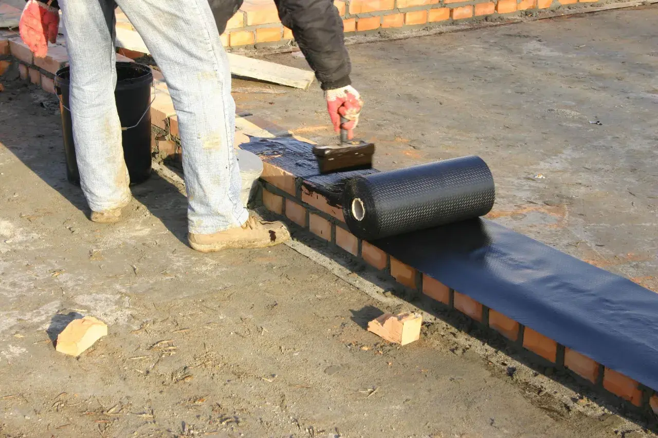 Pracownik nakłada na mur materiały hydroizolacyjne z rolki, zabezpieczając budynek przed wilgocią.