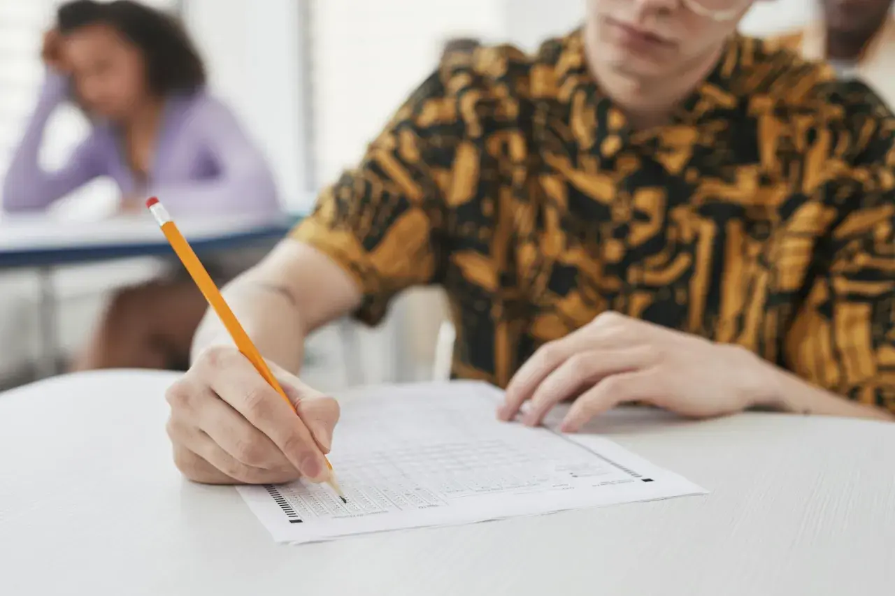 Uczeń pisze ołókiem na arkuszu testowym z wieloma polami wyboru.