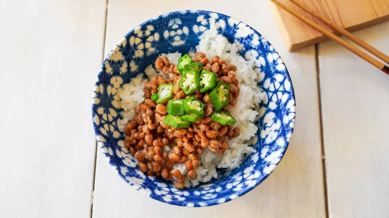 A bowl of natto with rice, topped with sliced okra. This healthy Japanese dish is ready to be enjoyed with chopsticks.