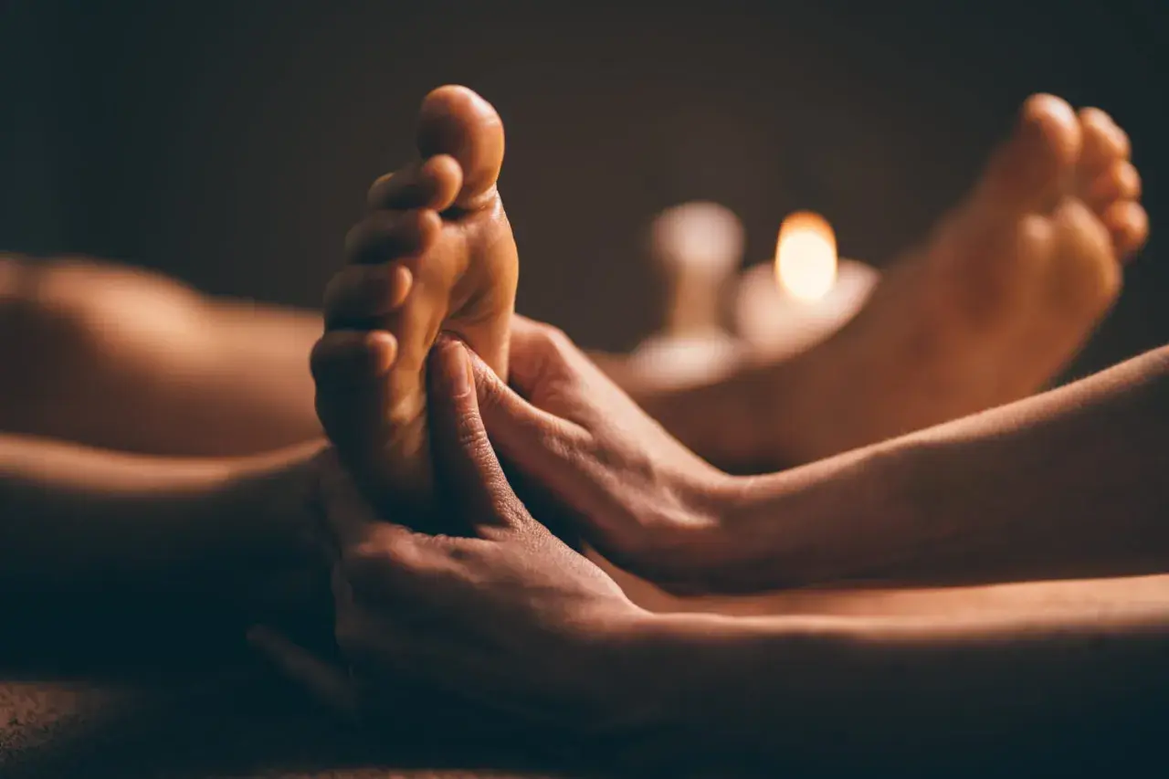 Mains expertes prodiguant un massage plantaire, révélant les bienfaits d'une détente profonde. Bougies tamisées en arrière-plan.