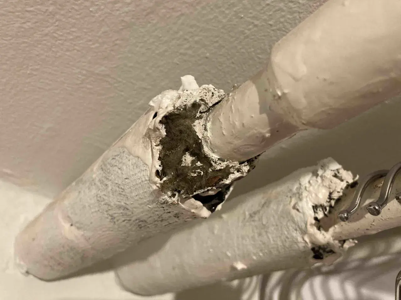 Skadad asbestisolering på rör. Materialet är vitt och smuligt, med synliga fibrer inuti.