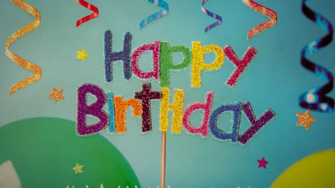 Kolorowe, brokatowe życzenia urodzinowe po angielsku "Happy Birthday" na tle serpentyn i gwiazdek.