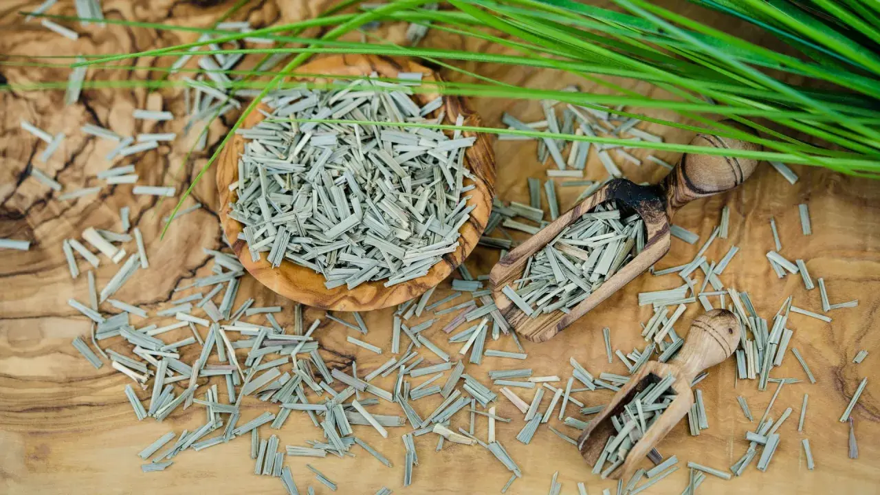Getrocknetes Zitronengras in einer Holzschale und Schaufeln, bereit zur Zitronengras Zubereitung. Frische grüne Halme liegen daneben.