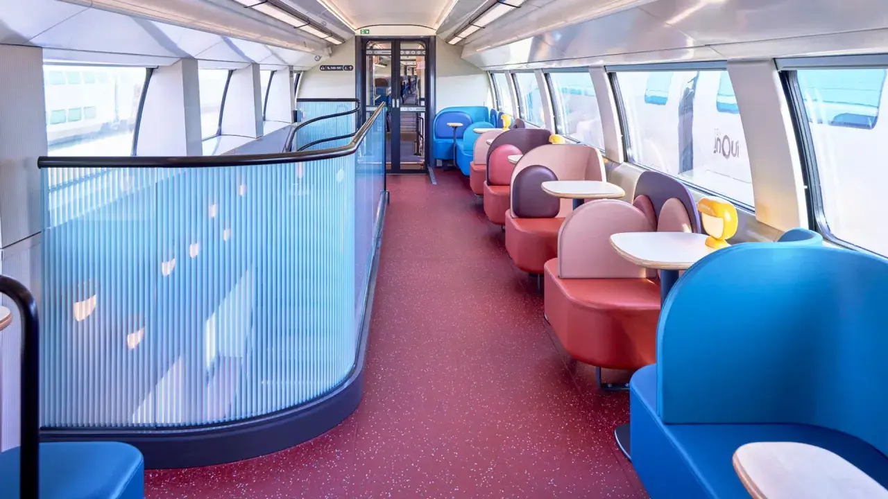Wnętrze pociągu TGV inOui z kolorowymi siedzeniami i stolikami.