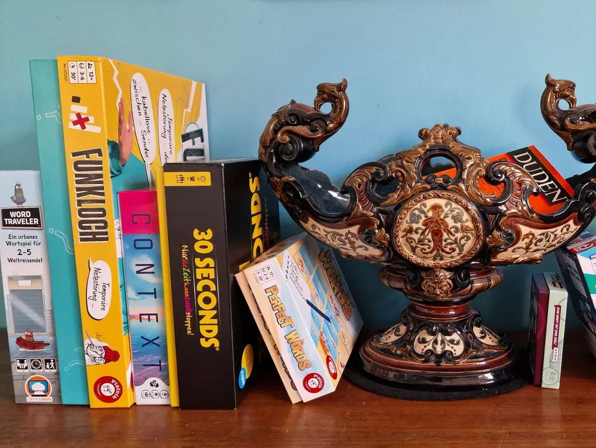 Brettspiele wie "Funkloch" und "30 Seconds" warten darauf, dass ihr Wort erraten wird. Ein Duden-Buch liegt daneben.