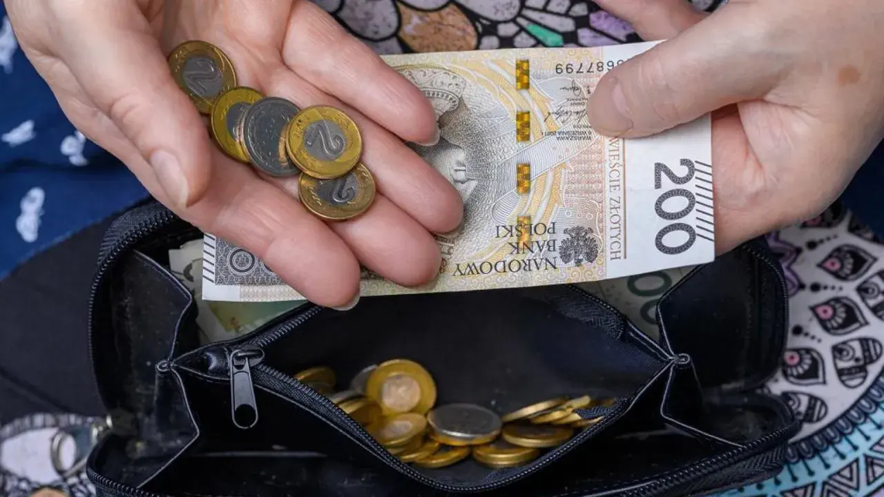 Dłonie trzymające polskie banknoty i monety nad otwartym portfelem.