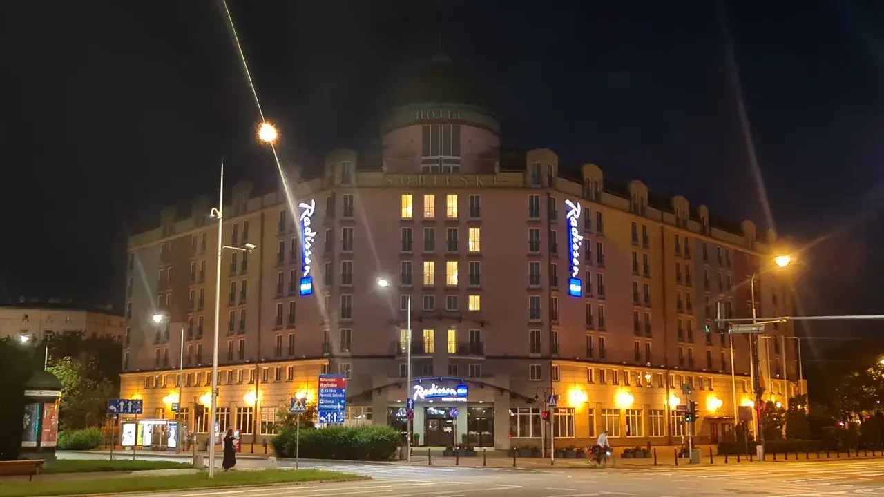 Nocą oświetlony Radisson Blu Sobieski Hotel Warsaw z neonami "Radisson" i napisem "HOTEL SOBIESKI".