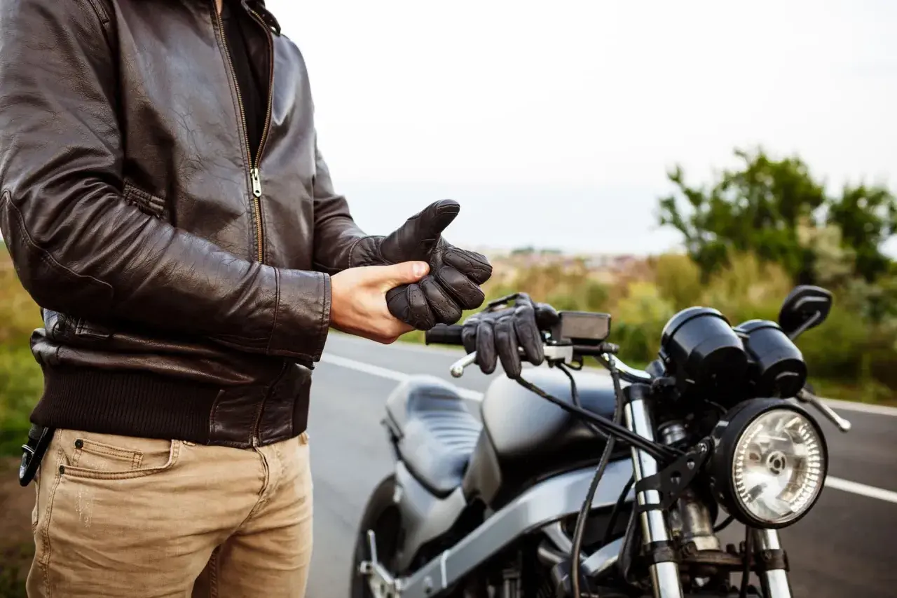 Hombre con chaqueta de cuero se pone guantes junto a una moto. ¿Listo para vender moto sin papeles?