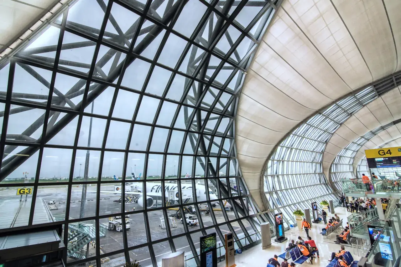 Moderne Architektur am Flughafen Bangkok: Flugzeuge stehen bereit, während Reisende im Wartebereich auf ihren Abflug warten.