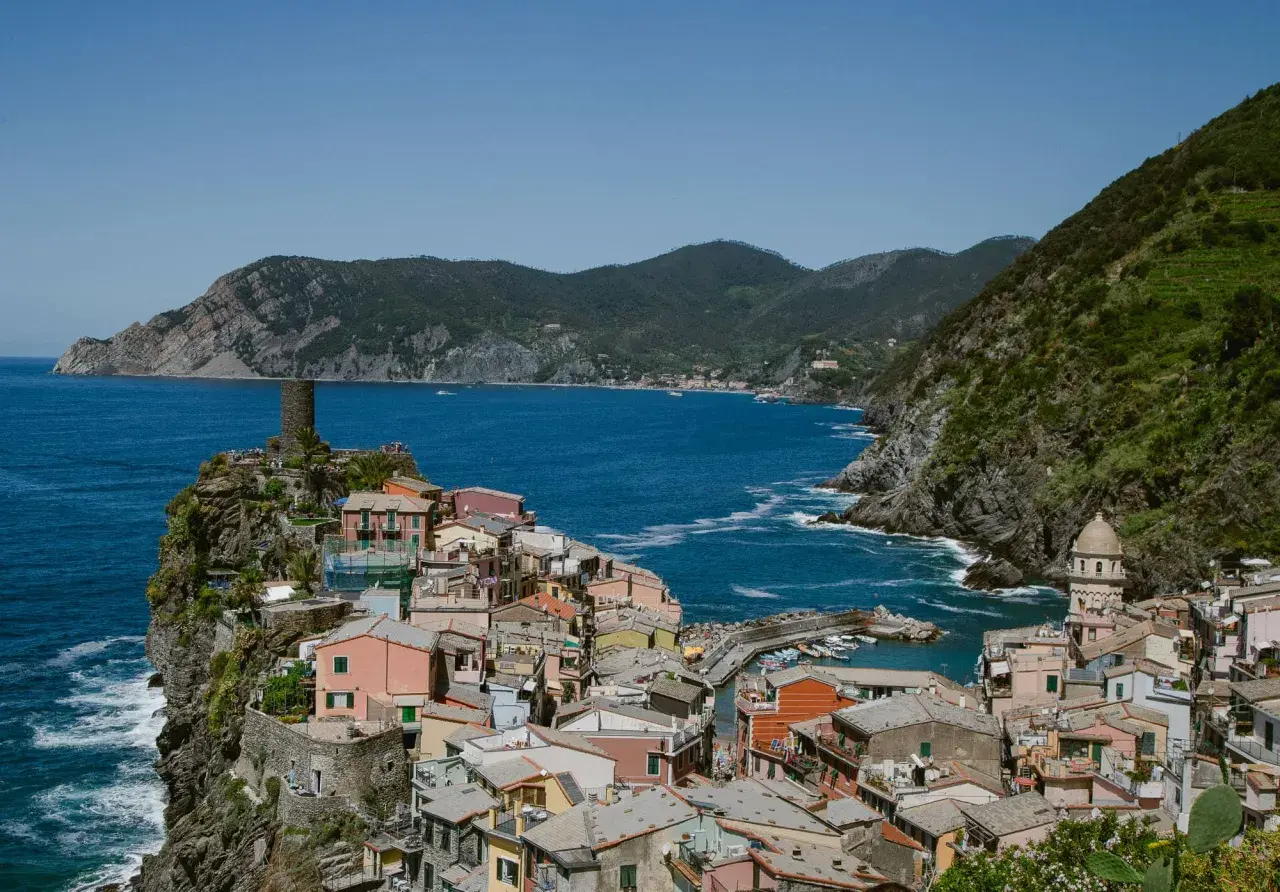Colorful houses cling to the cliffs of the Cinque Terre Italy coast, overlooking a vibrant blue sea. A medieval tower stands guard.