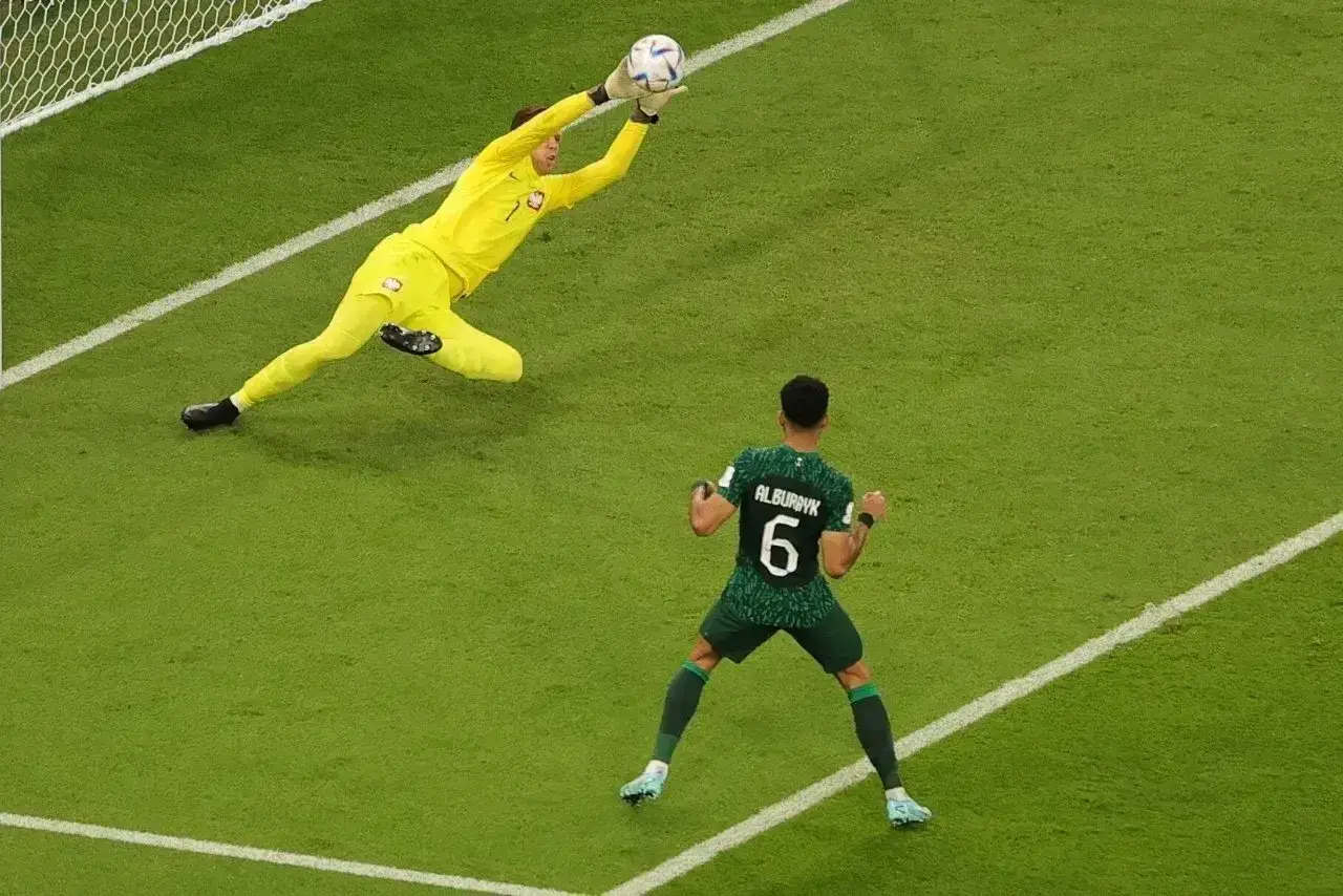 Bramkarz łapie piłkę po rzucie karnym dobitka po słupku. Piłkarz z numerem 6 cieszy się z akcji.