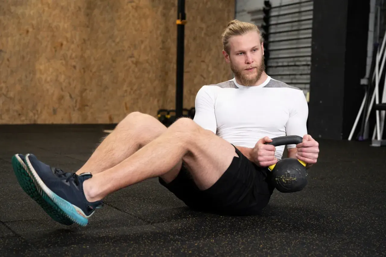 Mężczyzna wykonuje brzuszki z obciążeniem, trzymając kettlebell.