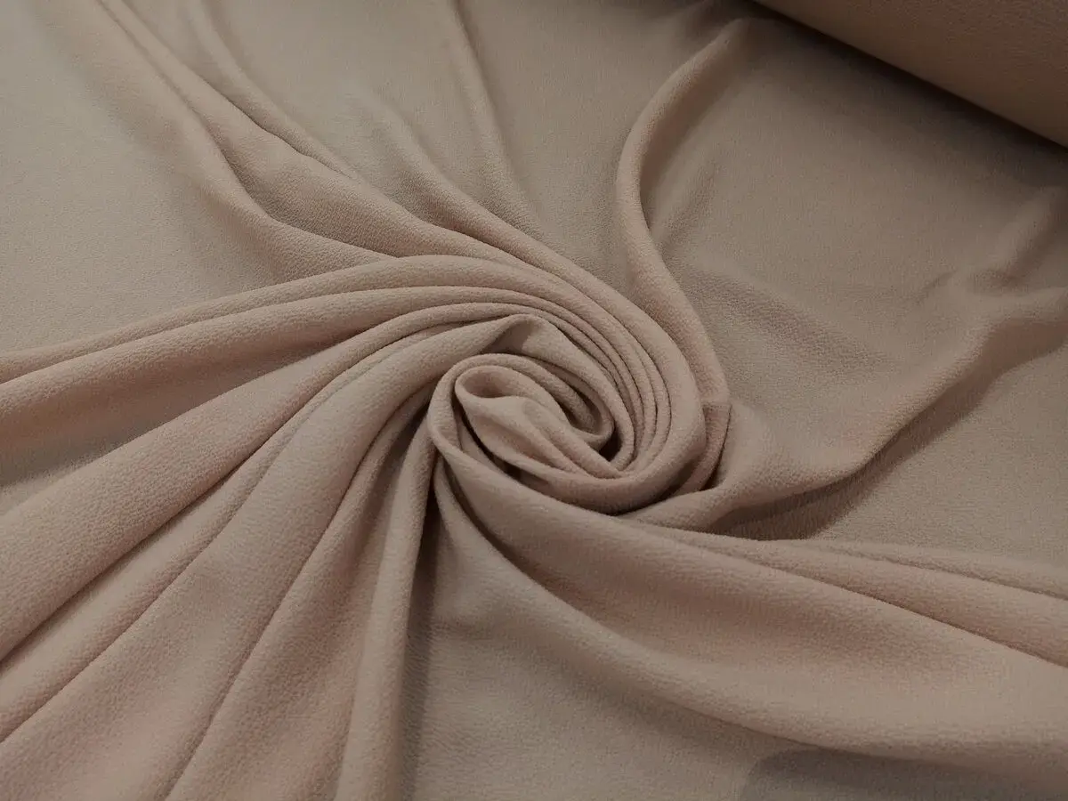 Delikatna, beżowa żorżeta układa się w miękkie fałdy, tworząc elegancką spiralę.