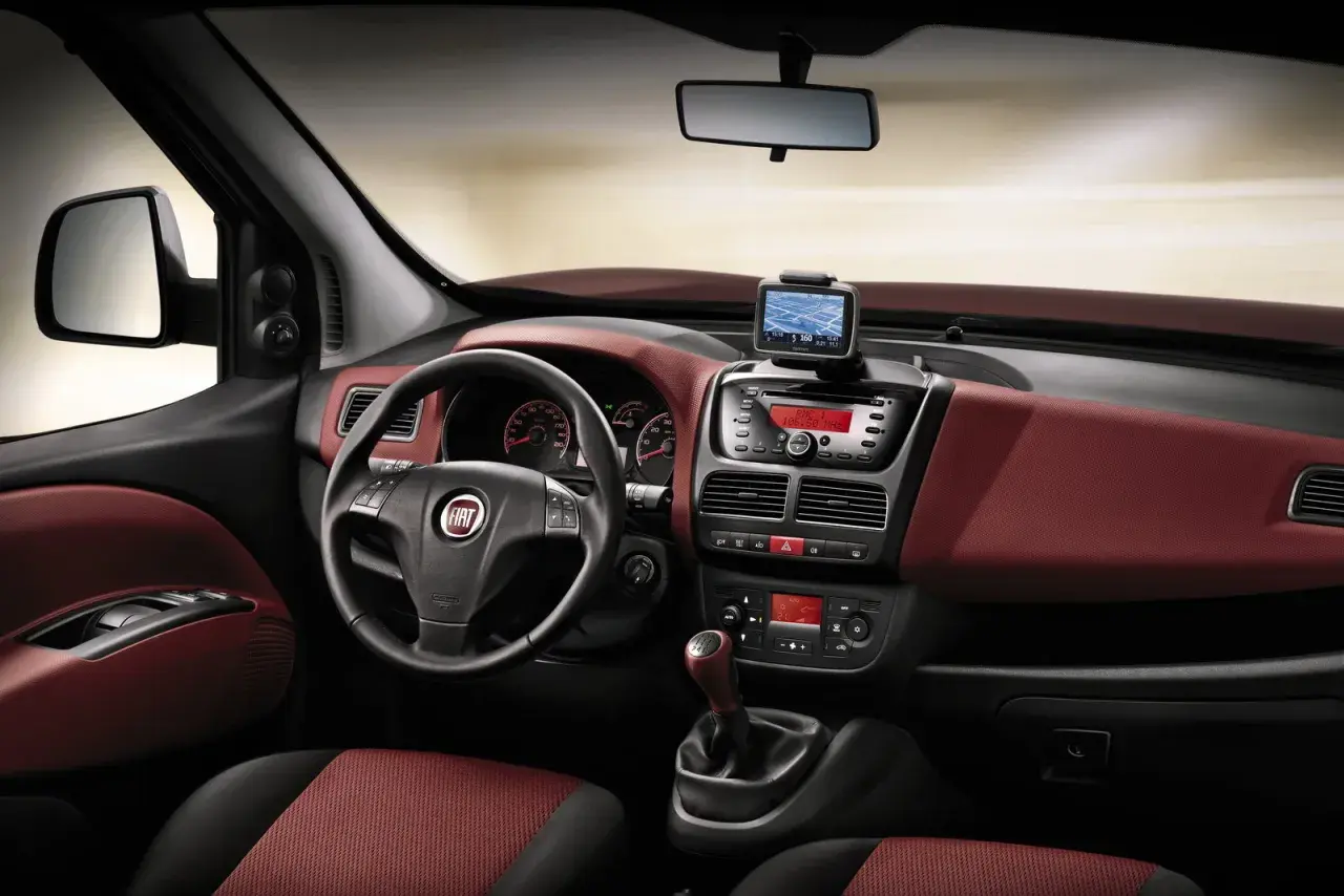 Interni Fiat Doblò con cruscotto rosso bordeaux, volante multifunzione, navigatore e radio.