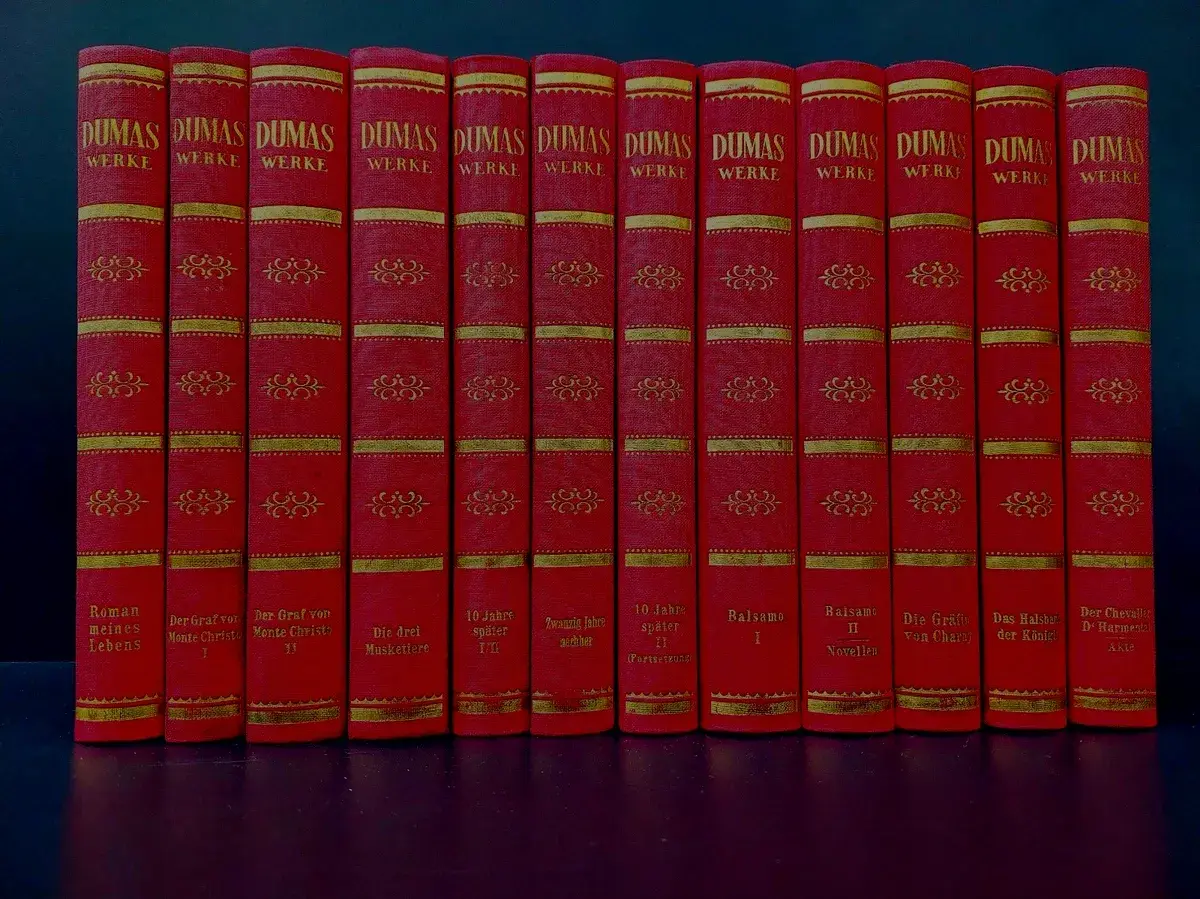 Eine Reihe roter Bücher mit goldener Verzierung, die Werke von Alexandre Dumas dem Älteren enthalten.