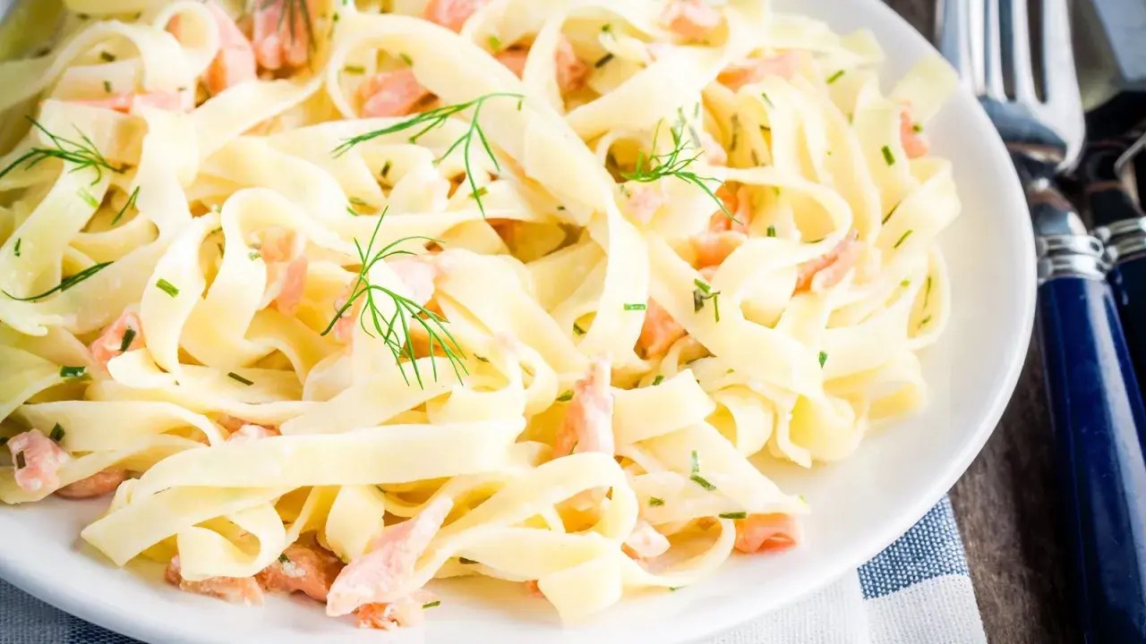 Tagliatelle mit Lachs, garniert mit Dill und Schnittlauch, auf einem weißen Teller. Ein köstliches Gericht, das zum Genießen einlädt.