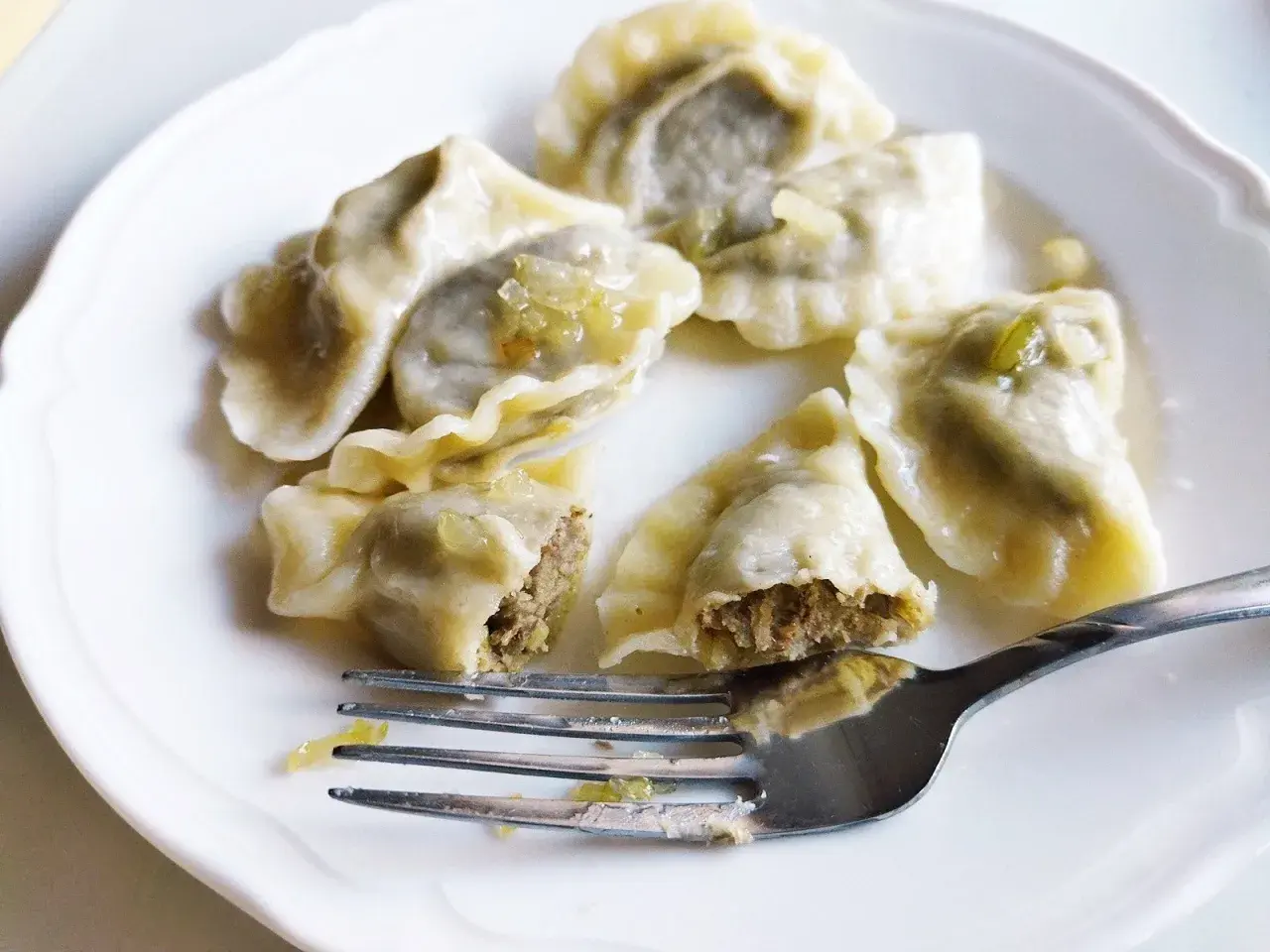 Pyszne pierogi z soczewicą na białym talerzu, jeden nadgryziony, obok widelec.