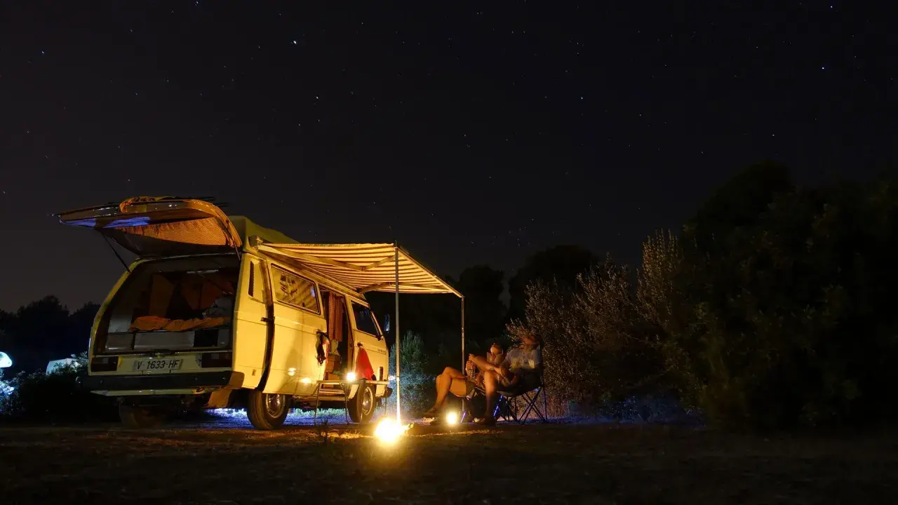 Sternenhimmel über einem Campervan mit ausgefahrener Markise. Ein Paar sitzt davor, die perfekte Mallorca Route für Camper.