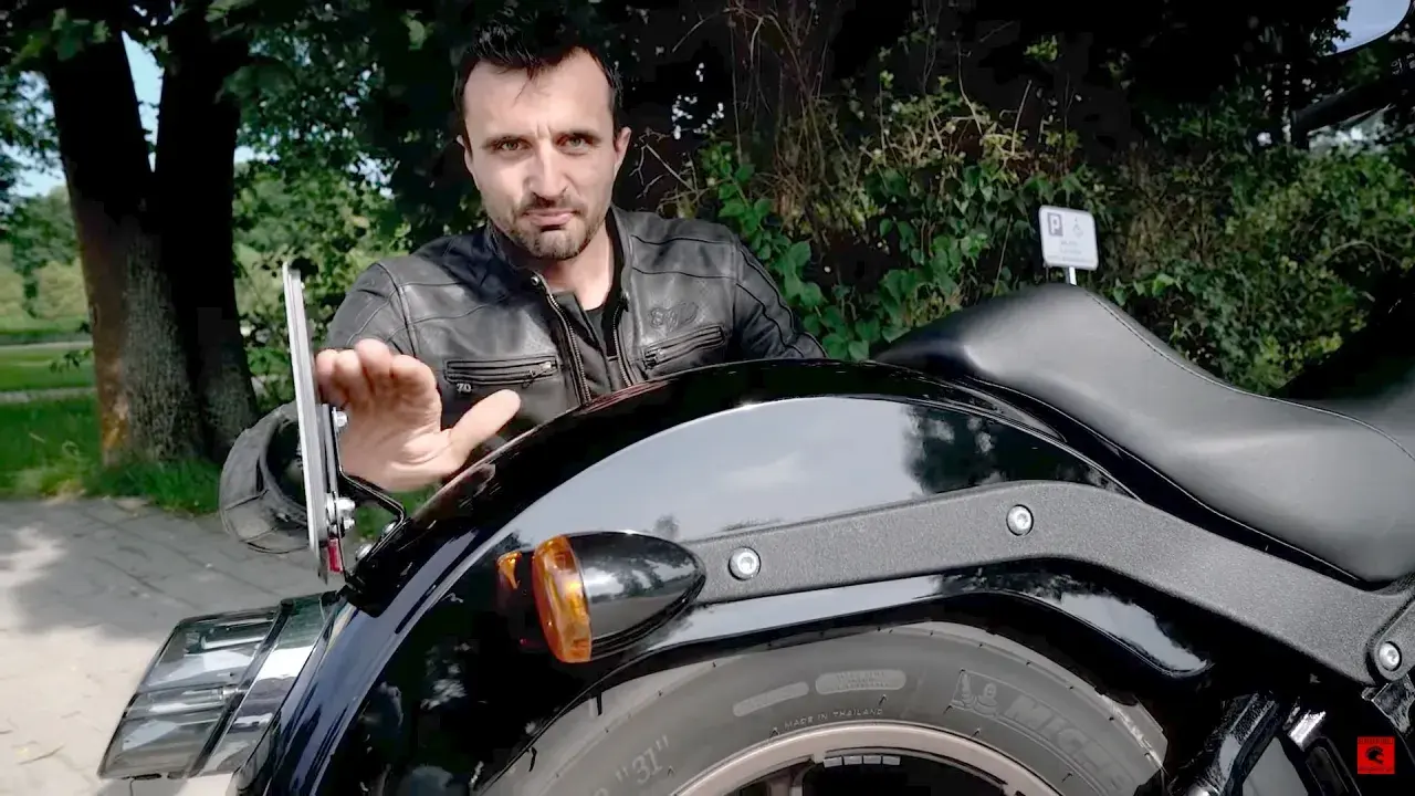 Mężczyzna w skórzanej kurtce pokazuje mocowanie tablicy motocyklowej.