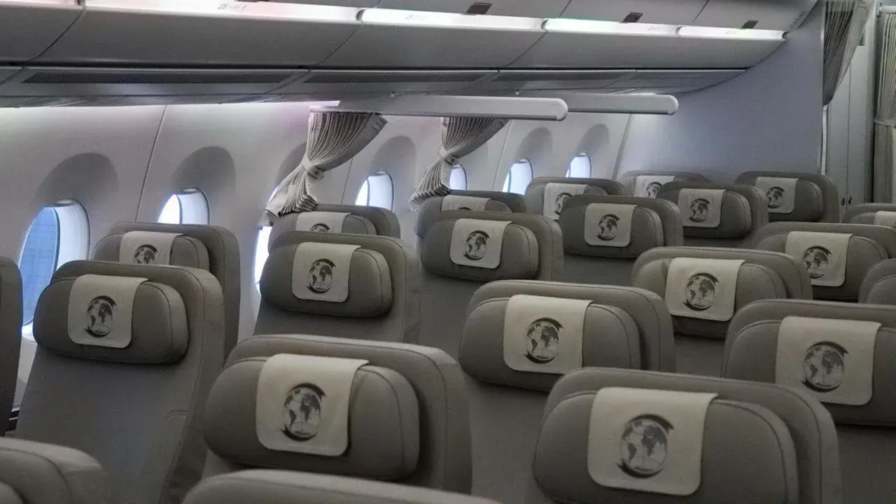 Innenansicht eines Flugzeugs mit Reihen von grauen Sitzen, die für den Bundeskanzler und seine Delegation reserviert sind. Jede Kopfstütze ziert ein Emblem mit der Weltkugel.