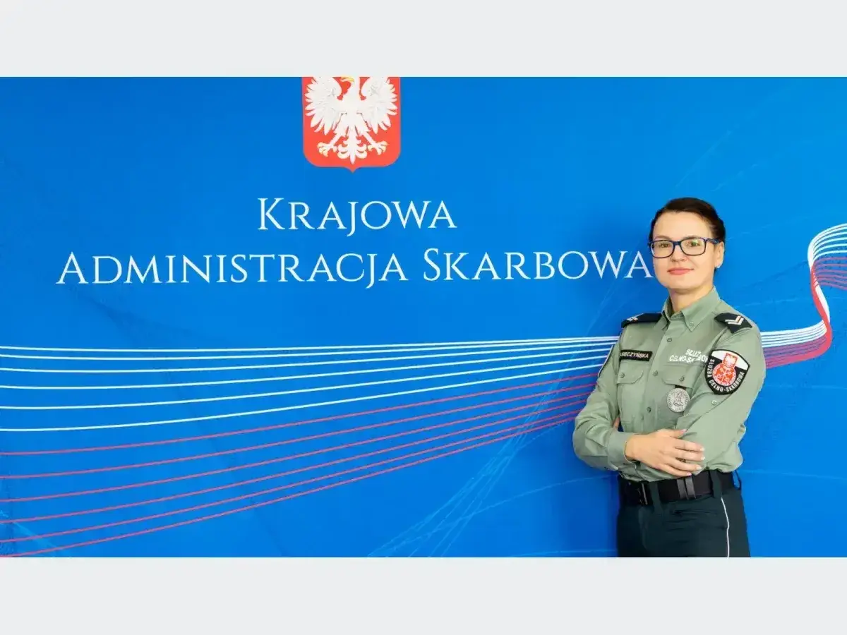 Kobieta w mundurze służby celno-skarbowej stoi przed niebieskim tłem z napisem "Krajowa Administracja Skarbowa".